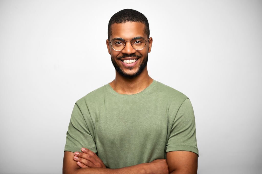 Close-up portrait of bearded businessman wearing black green t-shirt. Smiling handsome male executive is with black hair. Professional is against white background.